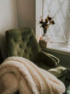a green chair with a blanket and a vase of flowers in front of it